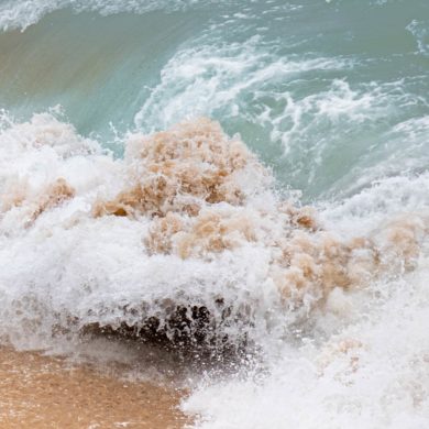 Olas del mar rompiendo en la orilla de una playa generando espuma. Poppyns Magazine