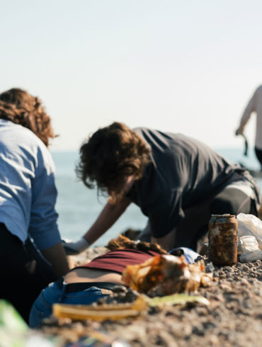 Personas agachadas recogiendo residuos en la playa entre las rocas. Poppyns Magazine