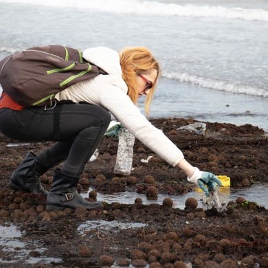 Mujer recogiendo plásticos en una playa. Poppyns Magazine