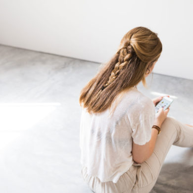 Chica sentada de espaldas mirando el móvil en una habitación de diseño minimalista con suelo de hormigón. Poppyns Magazine