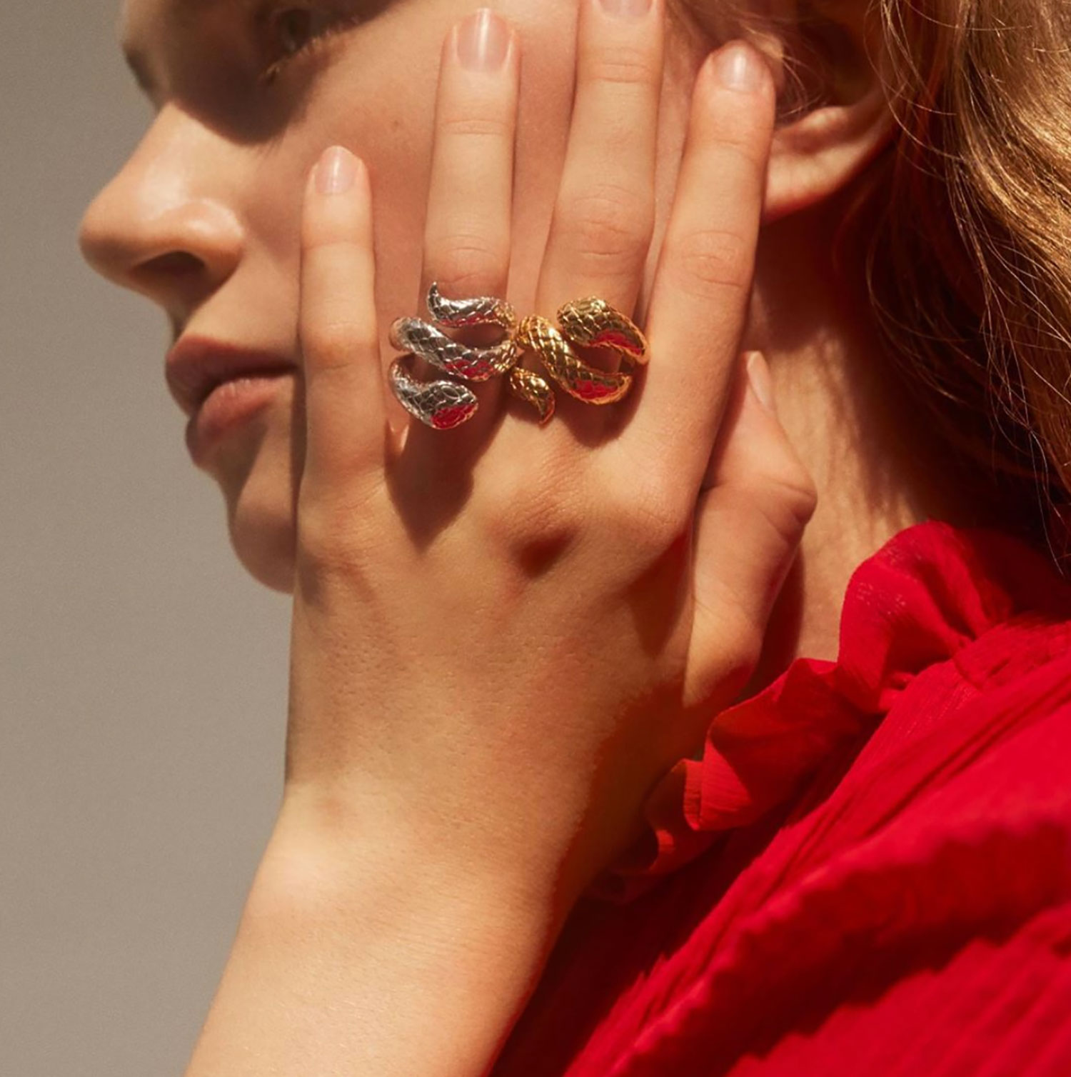 Mujer rubia con vestido rojo llevando dos anillos de serpientes de oro y plata en la mano. Poppyns Magazine
