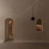 Interior de vivienda minimalista con paredes lisas en tono crema y suelo de microcemento, con una ventana y una puerta con arco ovalado. Poppyns Magazine