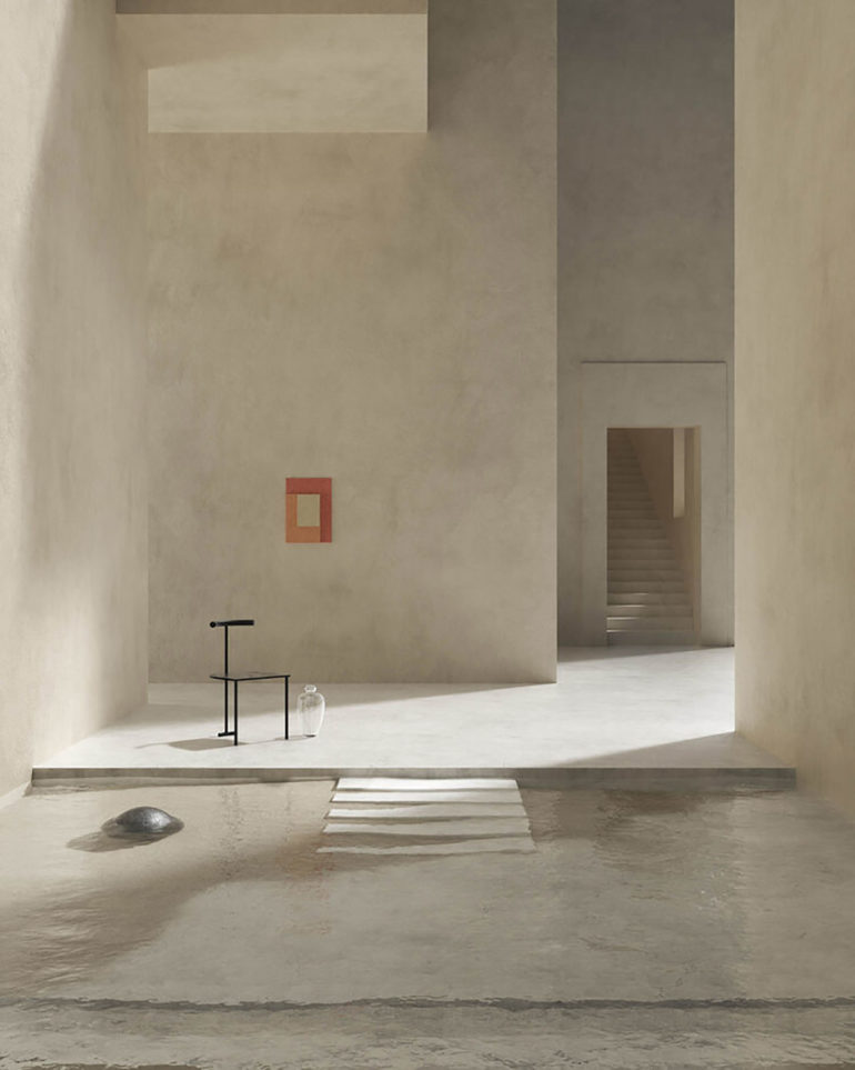 Interior de edificio con paredes de piedra lisas, un cuadro rojo sobre una pared, una puerta al fondo con unas escaleras ascendentes, una silla de forja junto a un jarrón de cristal y una piscina de agua clara con escalera de obra. Poppyns Magazine