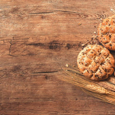 Hogaza de pan con semillas de trigo y sésamo junto a espigas de trigo sobre una mesa de madera. Poppyns Magazine