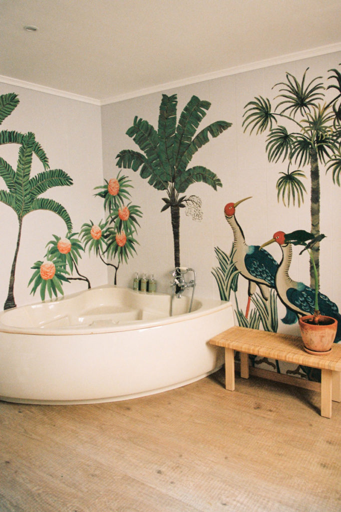 baño con bañera con pinturas en la pares de plantas y árboles Poppyns Magazine