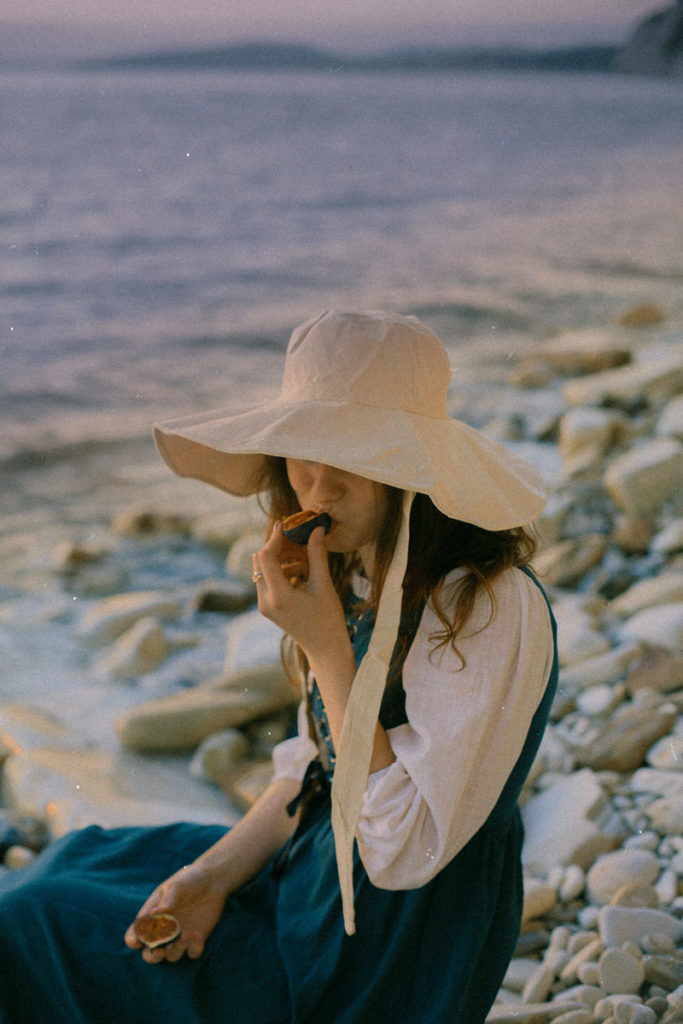 Mujer con sombrero en playa comiendo despacio un higo
