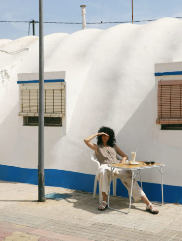 Mujer sentada en mesa al sol con refresco.